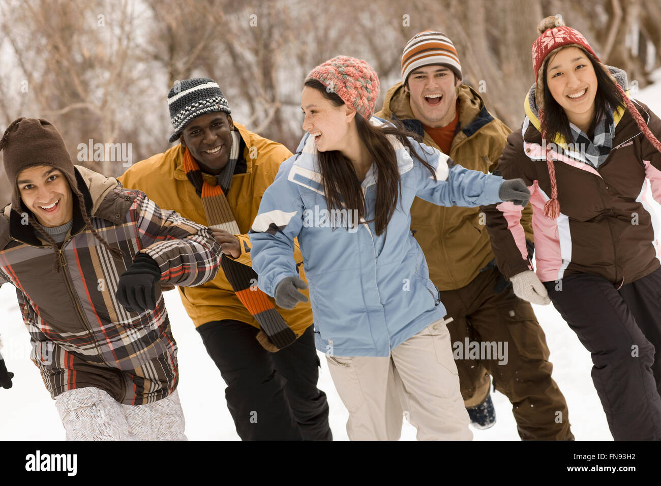 Five young people, men and women running across the snow. Stock Photo