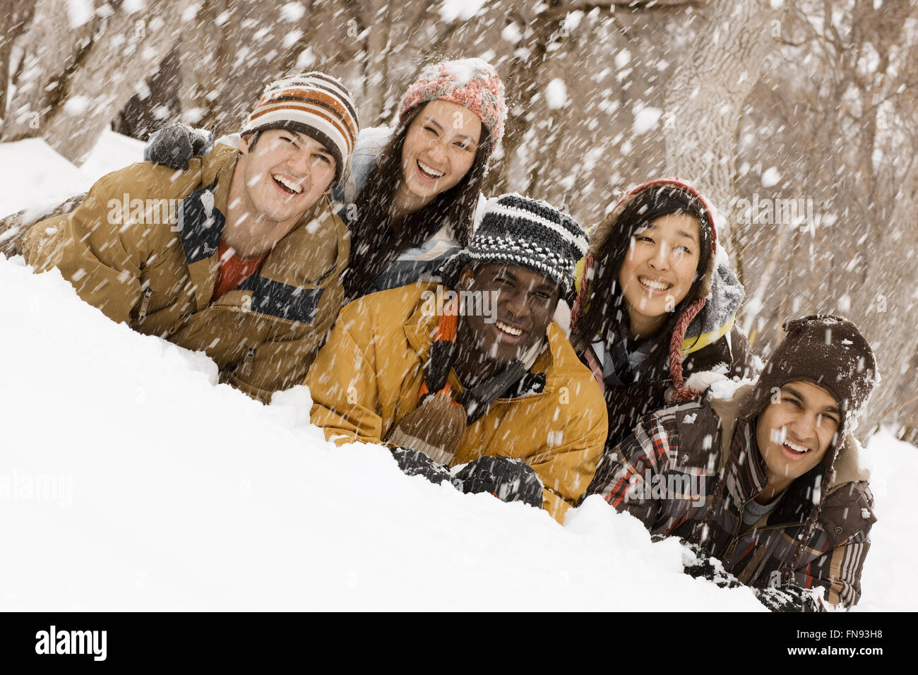Five young people lying on the snow laughing. Snow falling. Stock Photo