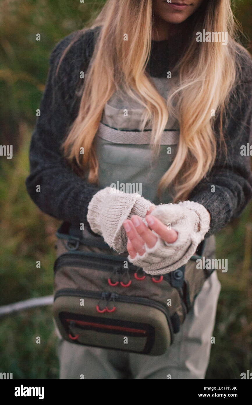 A woman with long blonde hair putting on woollen fingerless mittens. Stock Photo