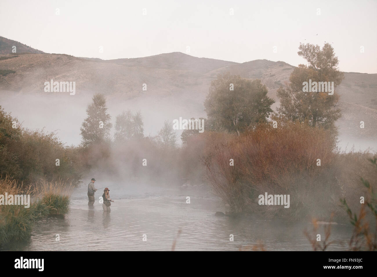 A couple, a man and woman standing in mid stream fly fishing in a river. Stock Photo