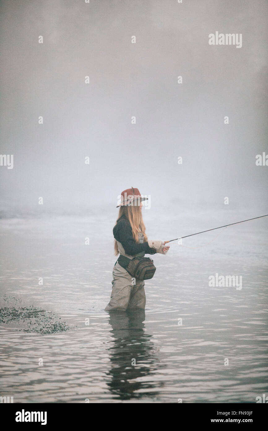 A woman fisherman fly fishing, standing in waders in thigh deep water. Stock Photo