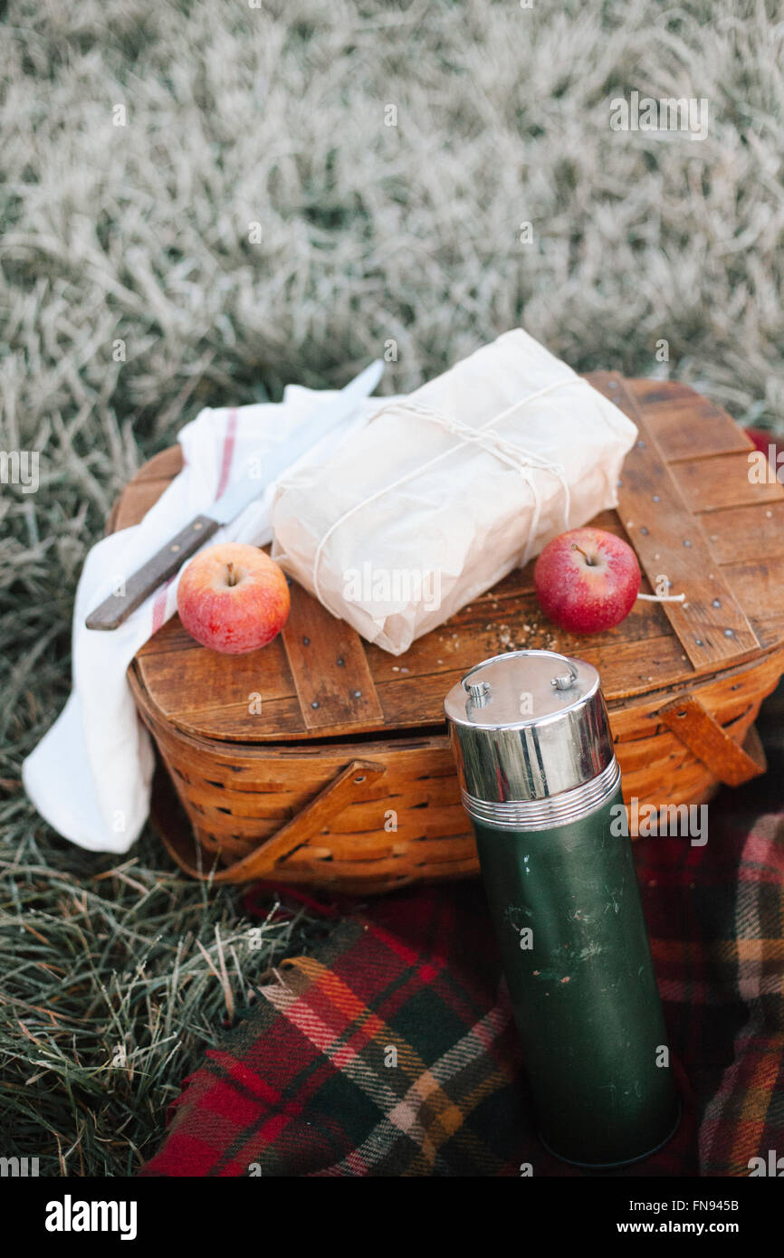 A winter picnic, apples and a wrapped cake by a fishing basket on a rug. Stock Photo