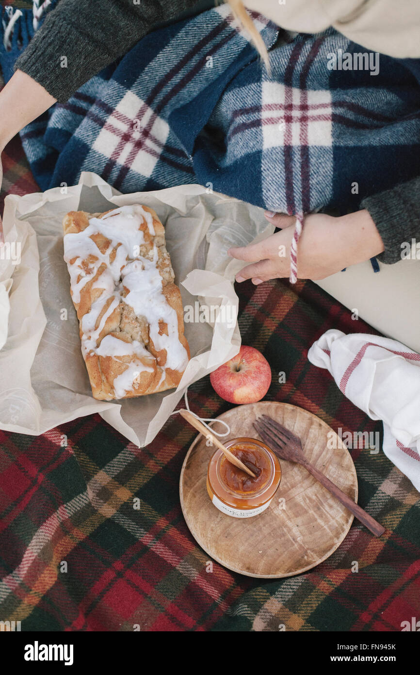 View from overhead of two people at a picnic, one unwrapping a loaf cake. Stock Photo