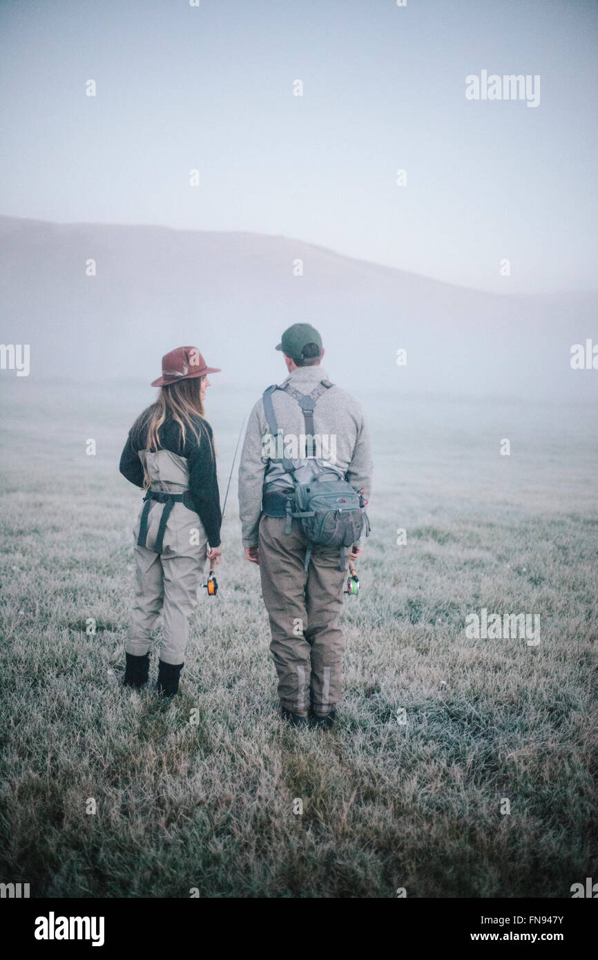 Two people walking across a meadow in early morning mist carrying