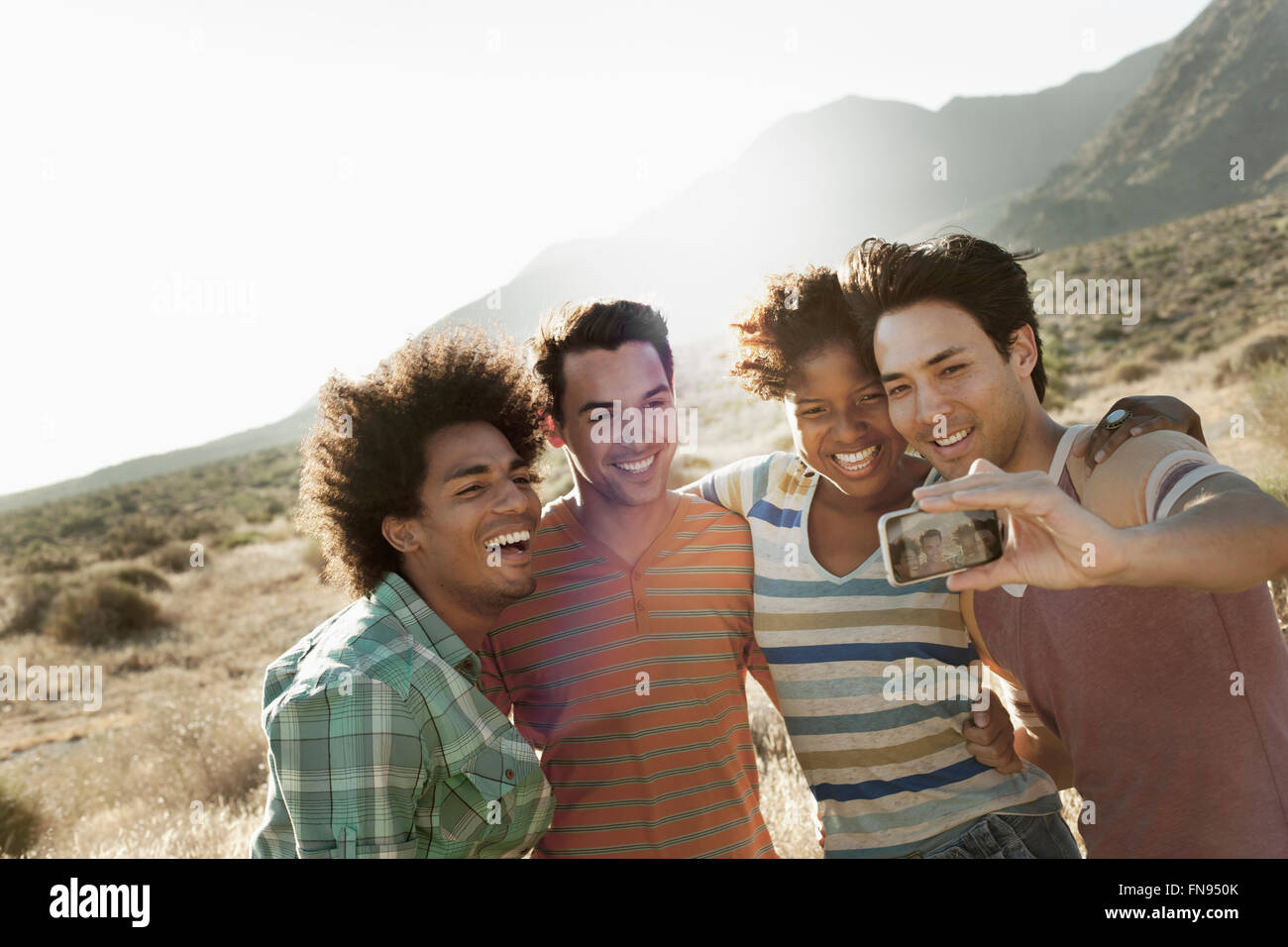 A group of friends, men and women, heads together posing for a selfy in the heat of the day. Stock Photo