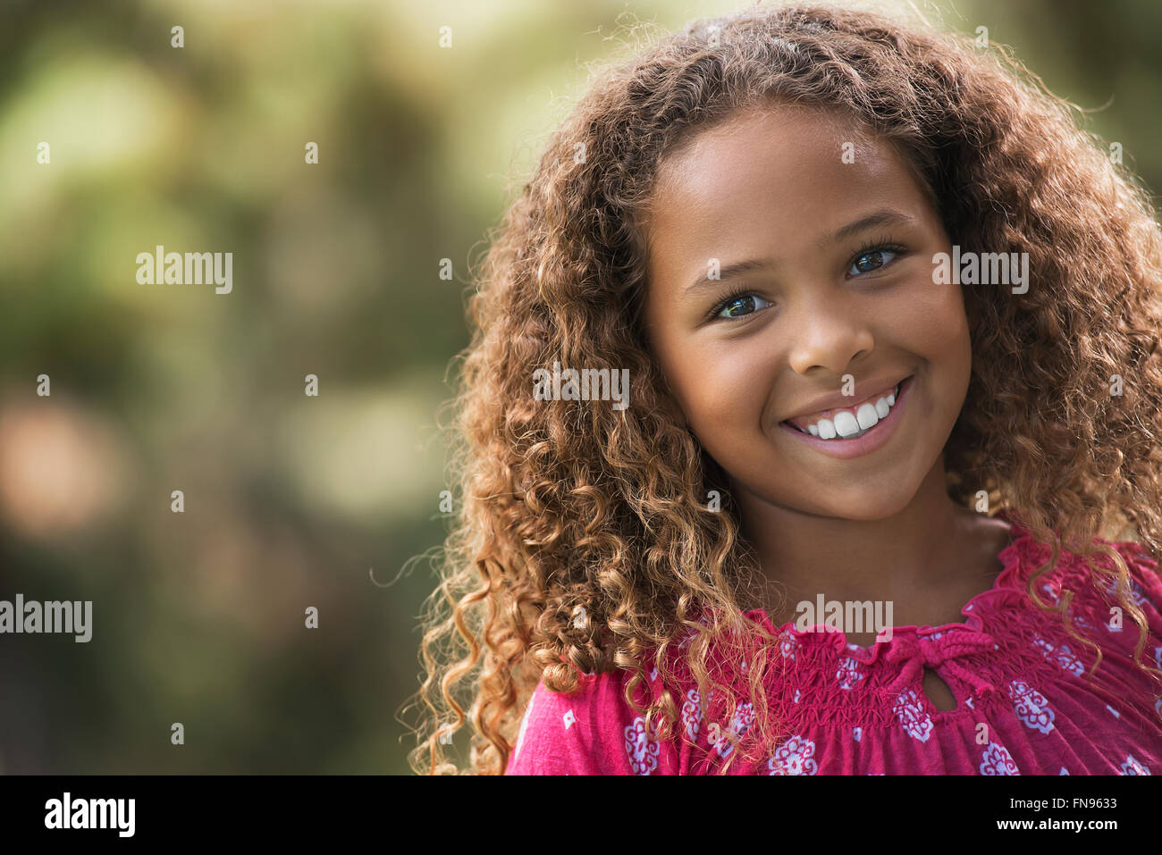 A young girl in a pink dress with long brown curly hair Stock Photo - Alamy
