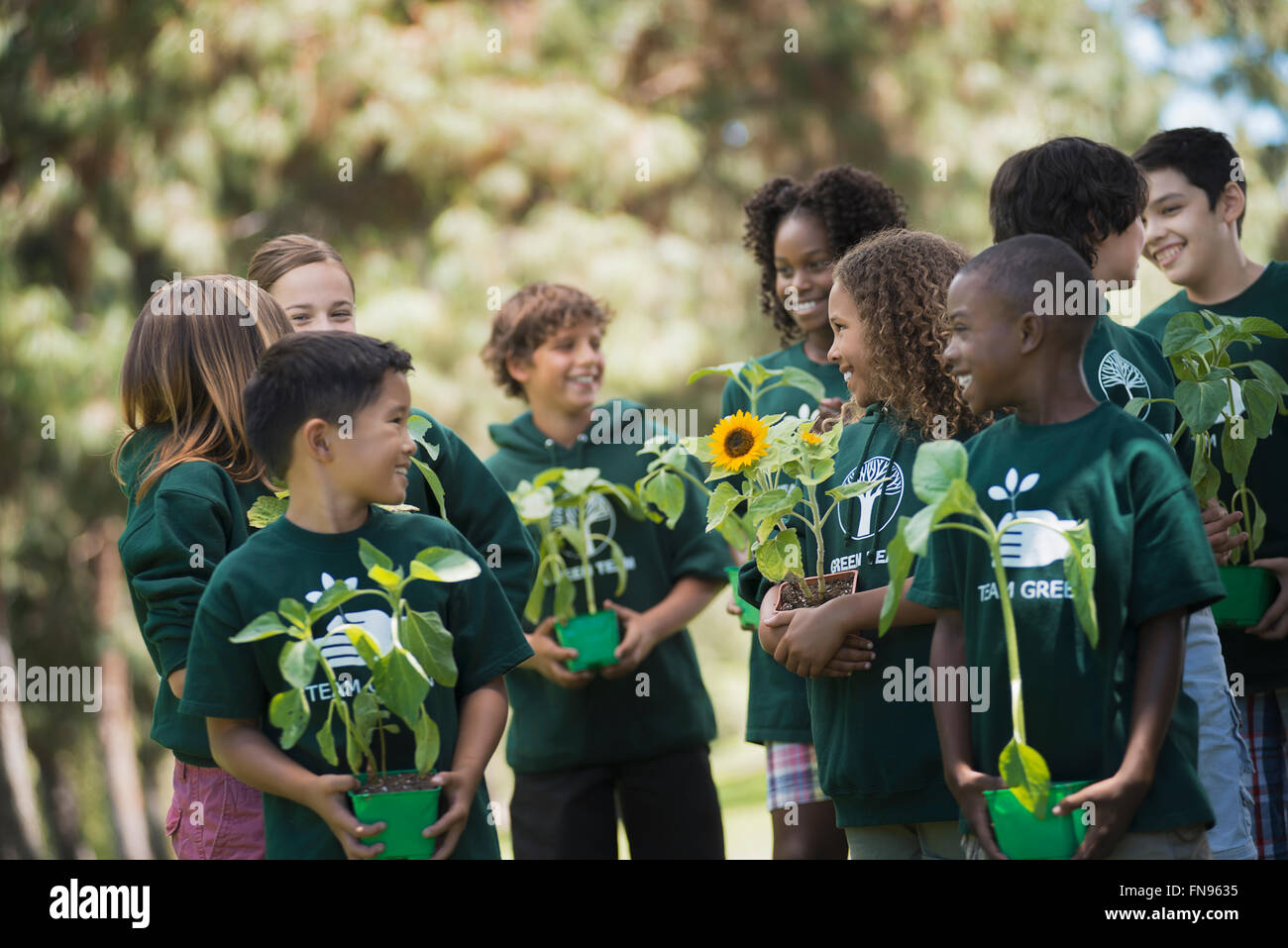 Children in a group learning about plants and flowers, carrying plants and sunflowers. Stock Photo