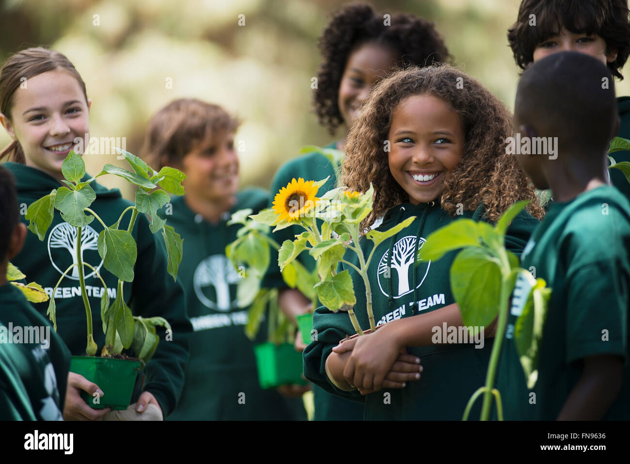 Children in a group learning about plants and flowers, carrying plants and sunflowers. Stock Photo