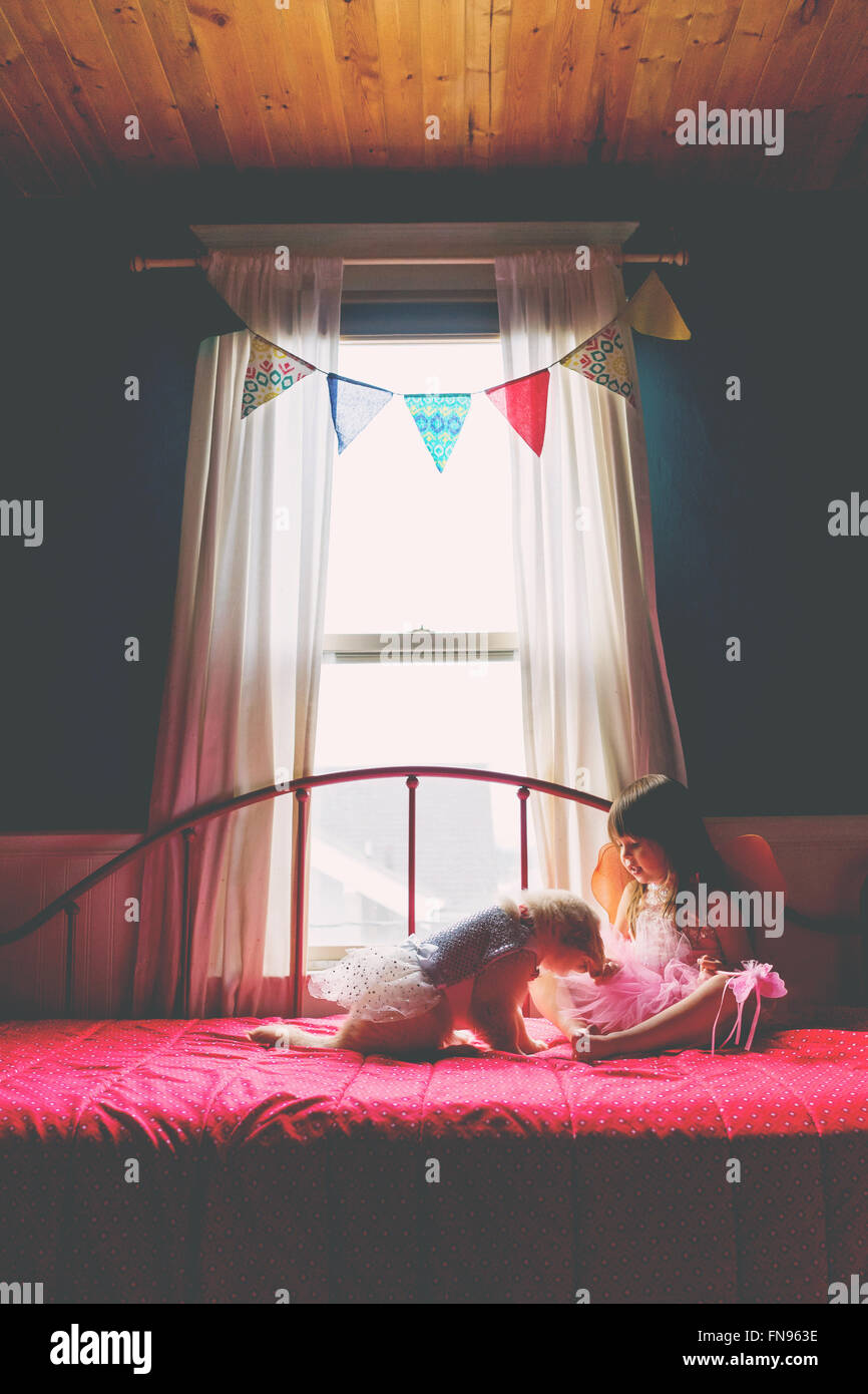 Girl sitting on bed playing with golden retriever puppy dog Stock Photo ...