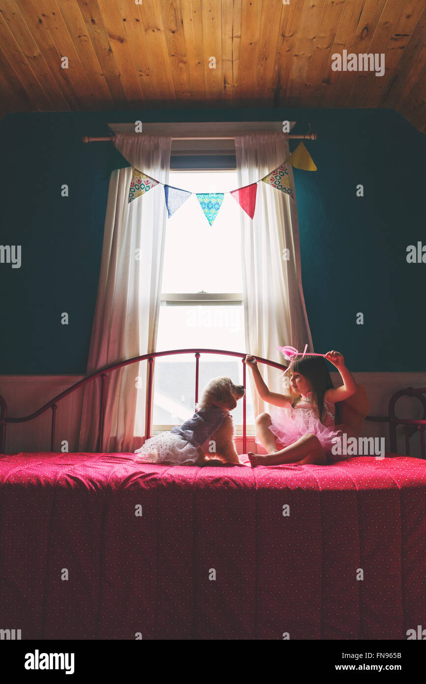 Girl sitting on bed playing with golden retriever puppy dog Stock Photo ...