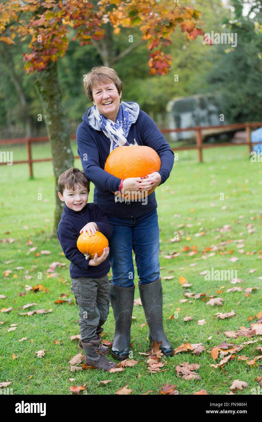 A mature woman and a small boy holding pumpkins, large and small. Stock Photo