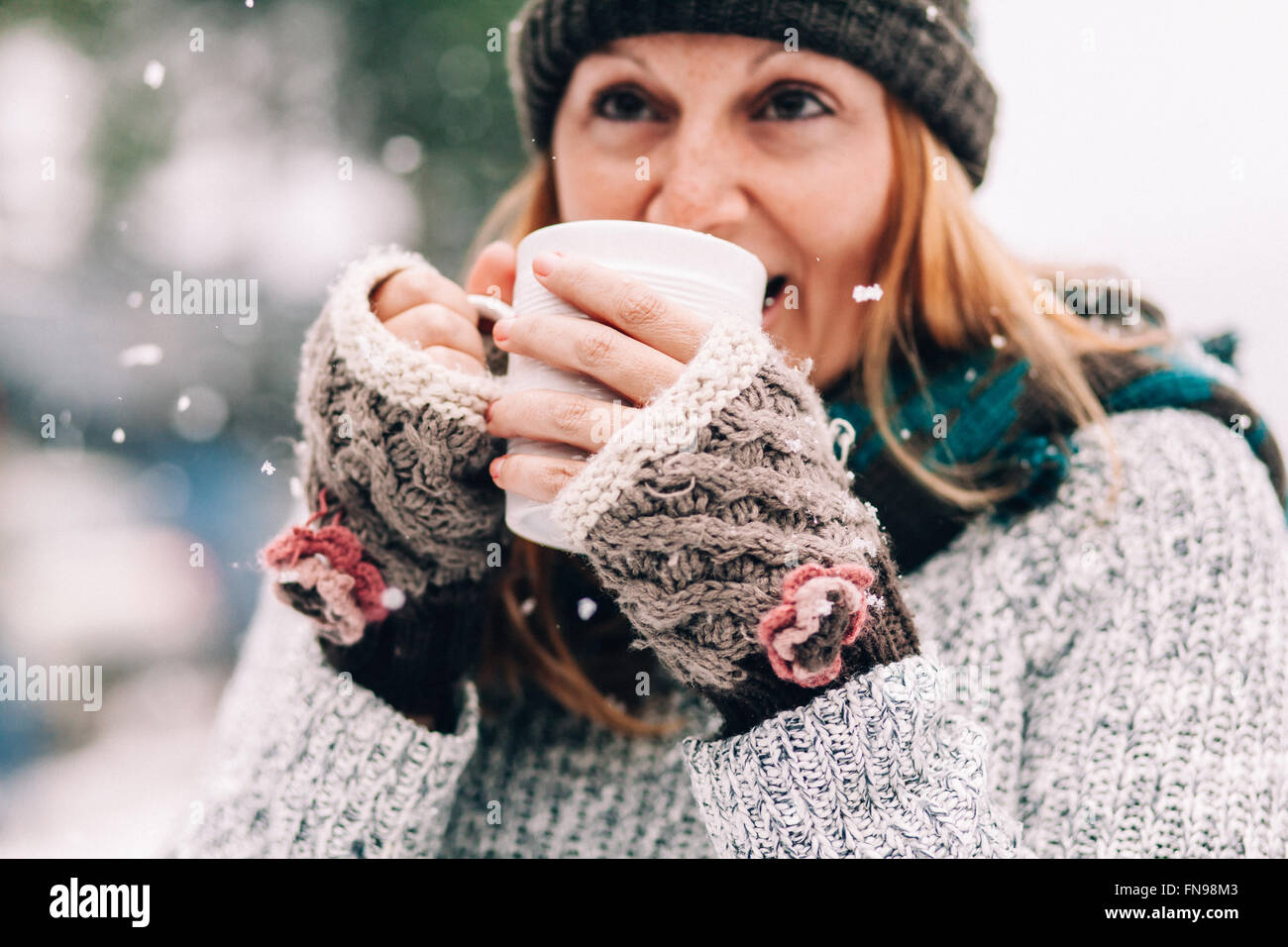 Woman standing in snow holding hot drink Stock Photo