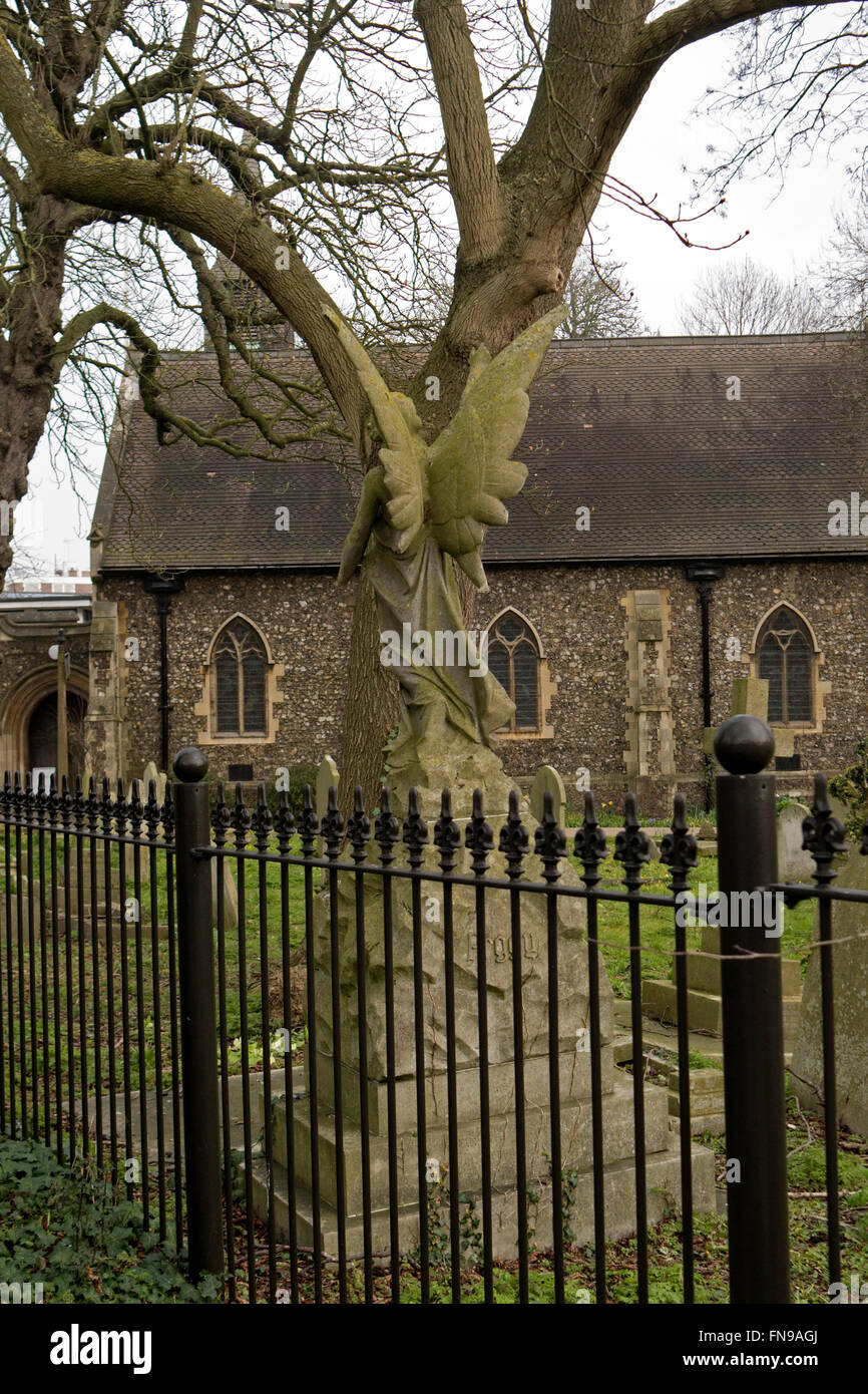 A gravemarker statue of an angel in a churchyard camouflaged by the limbs of a tree. Stock Photo