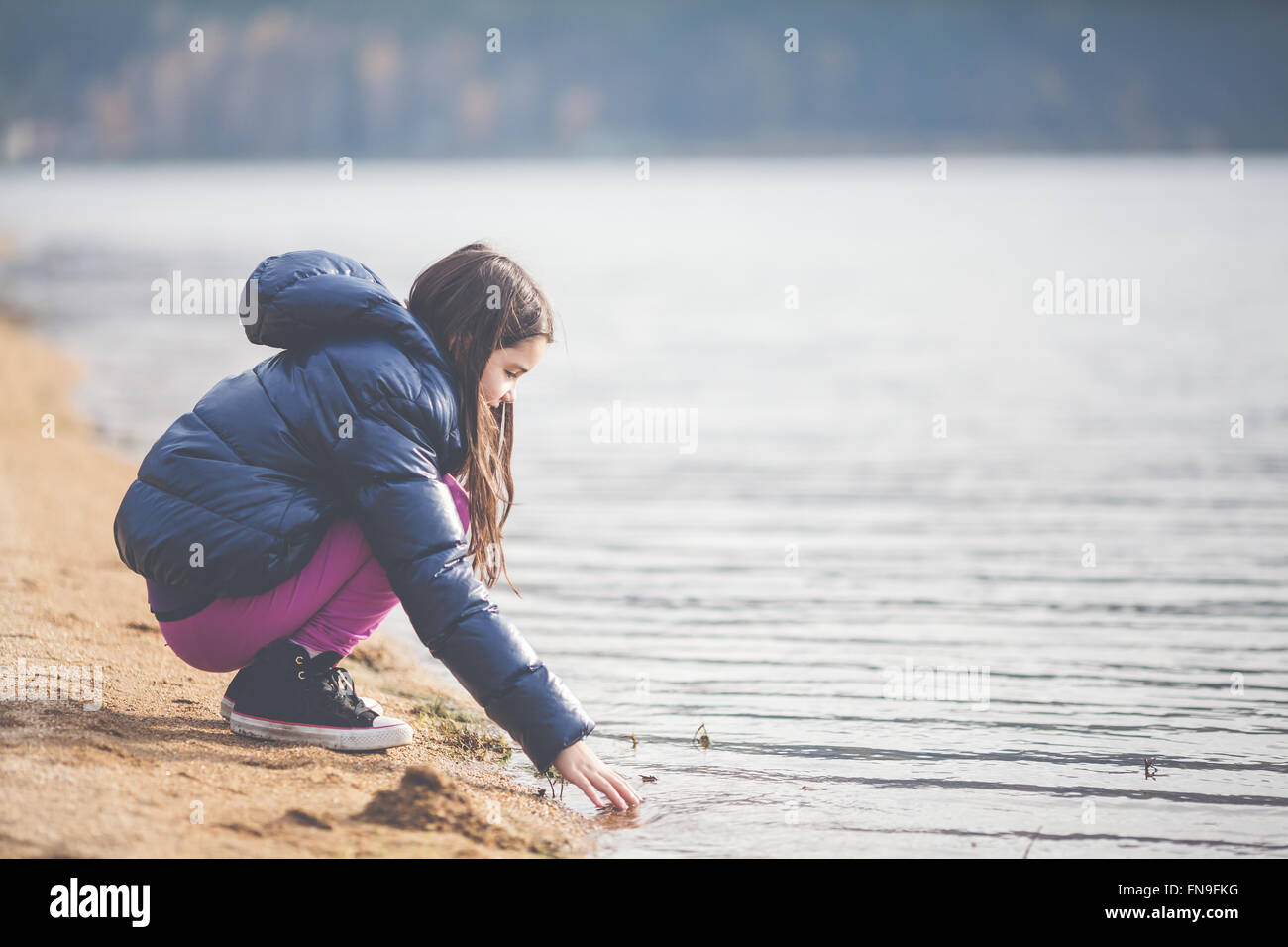 Girl crouching by a lake Stock Photo