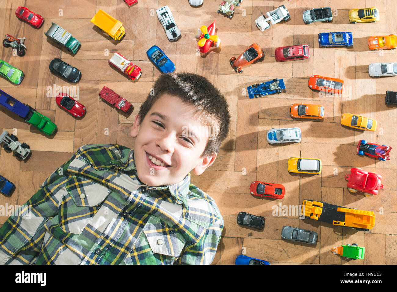 Boy lying on floor surrounded by toy cars Stock Photo