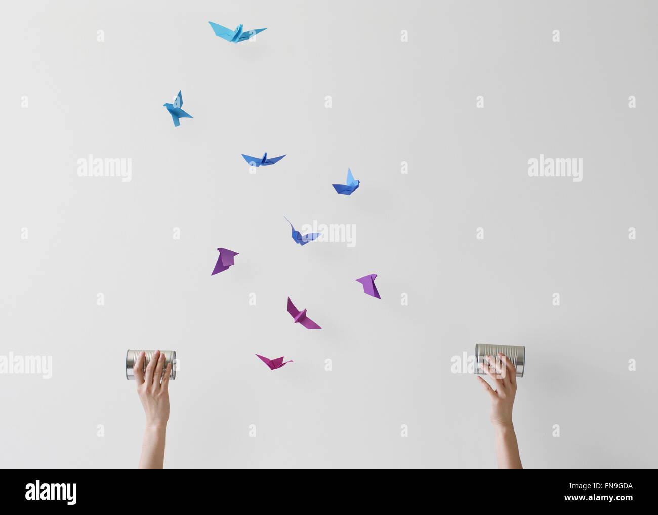Woman holding wireless tin can phones with conceptual birds flying mid air Stock Photo