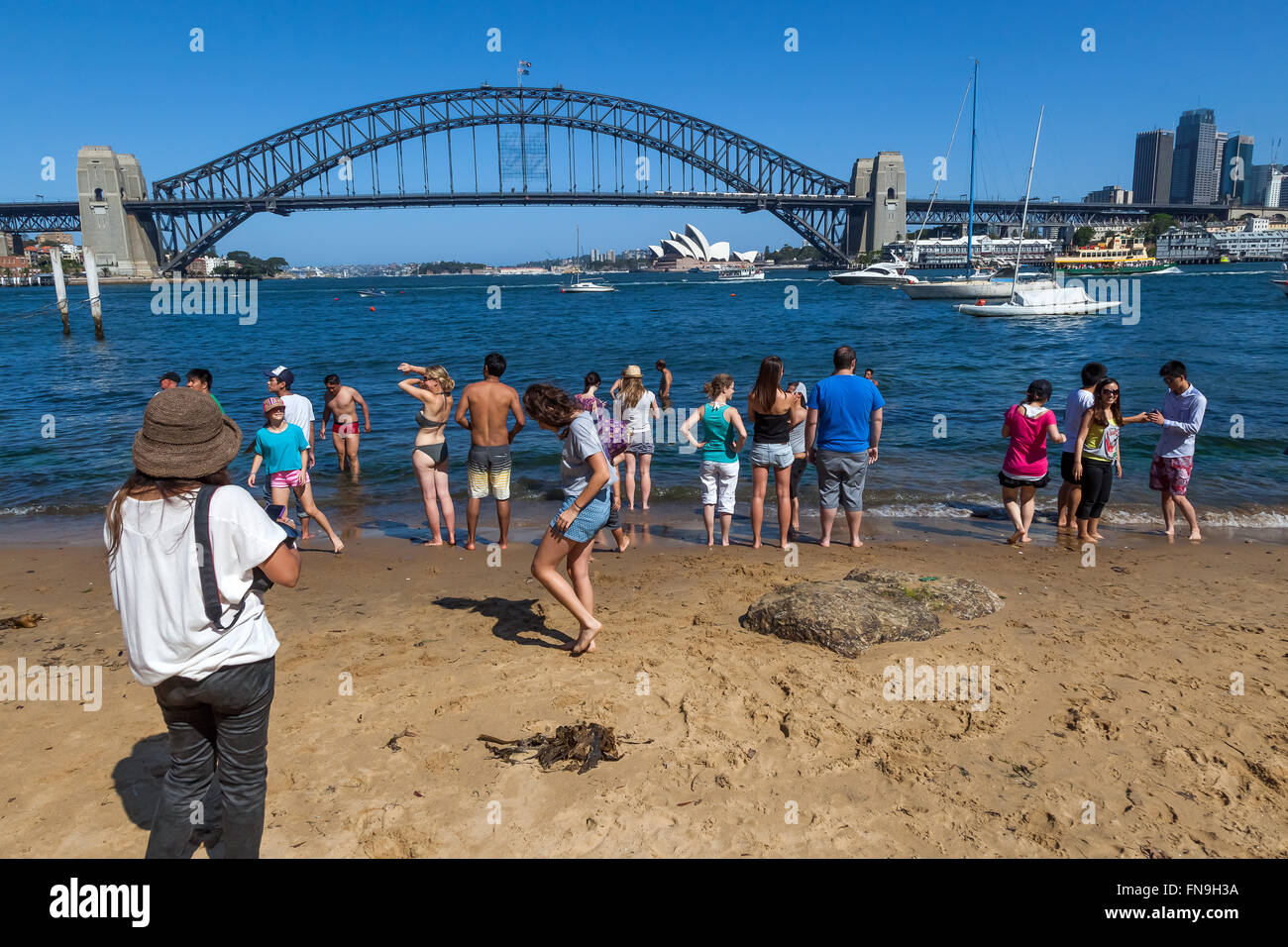 Tourists on the beach viewing Sydney Opera House and the Harbor Bridge in Sydney, Australia. Stock Photo