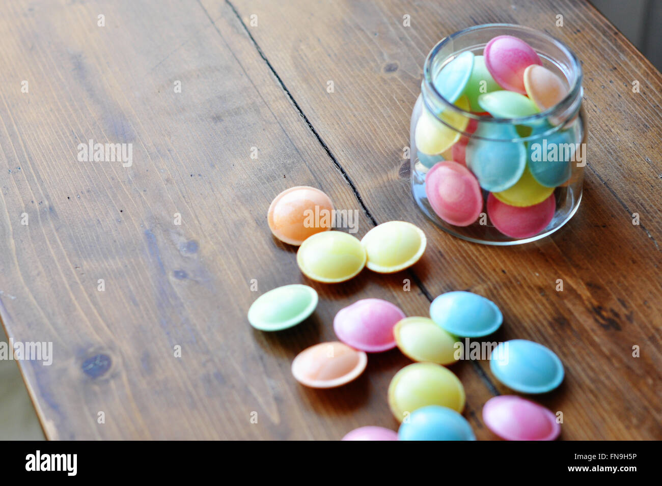 Jar of Pastel colored flying saucer sweets on wooden table Stock Photo