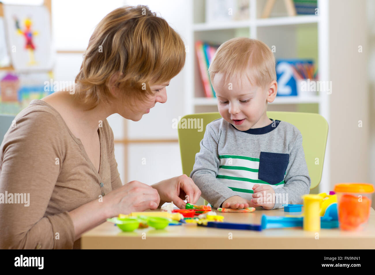 Woman and kid boy playing with plasticine at table in nursery room Stock Photo