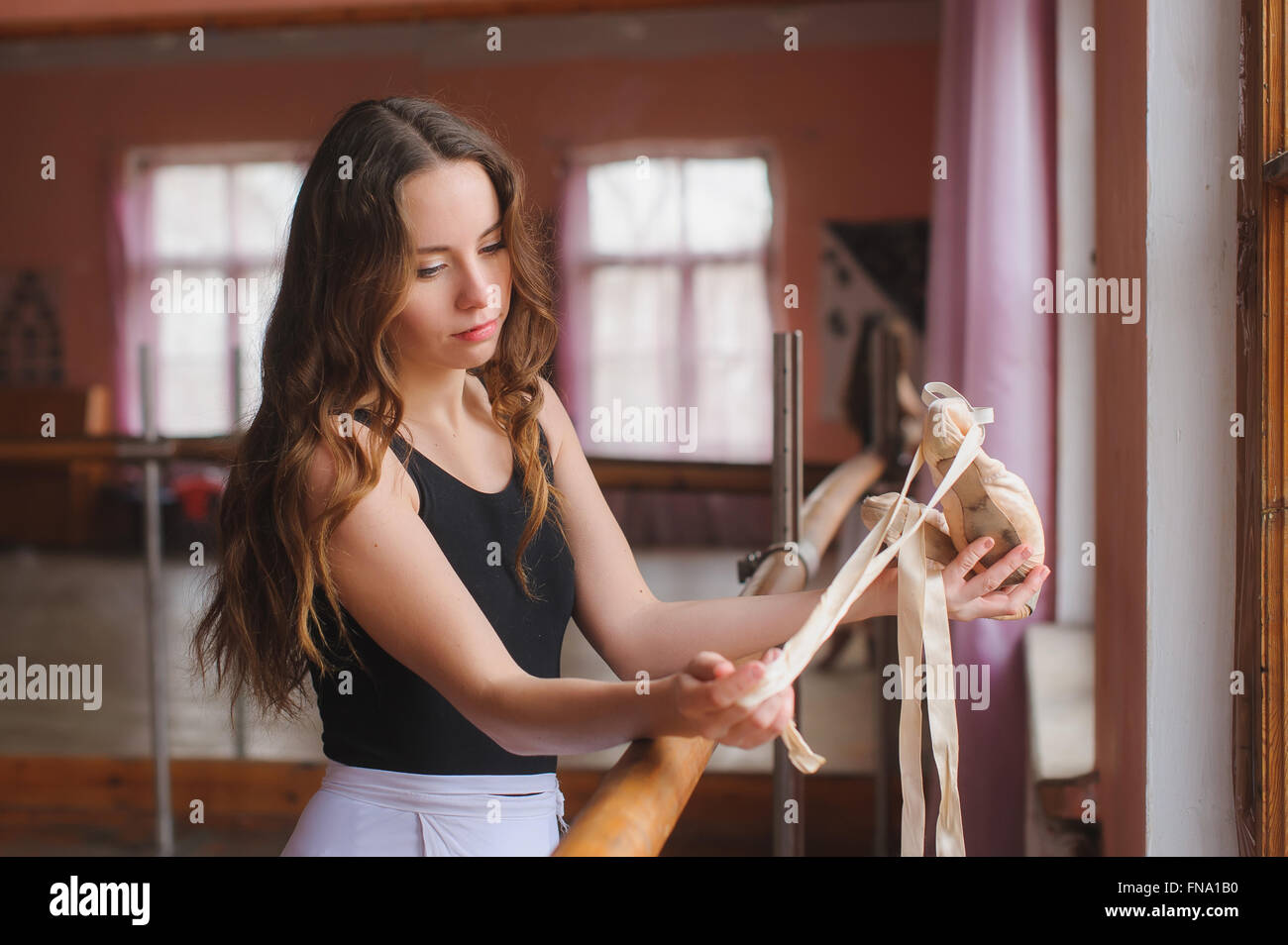 Young ballerina dancer girl standing at ballet barre looks at their