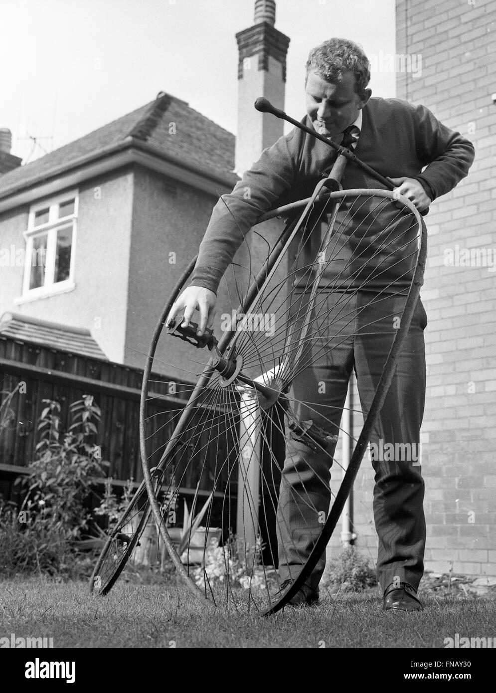 Man with penny farthing bicycle in need of repair with a buckled wheel 1960s Stock Photo