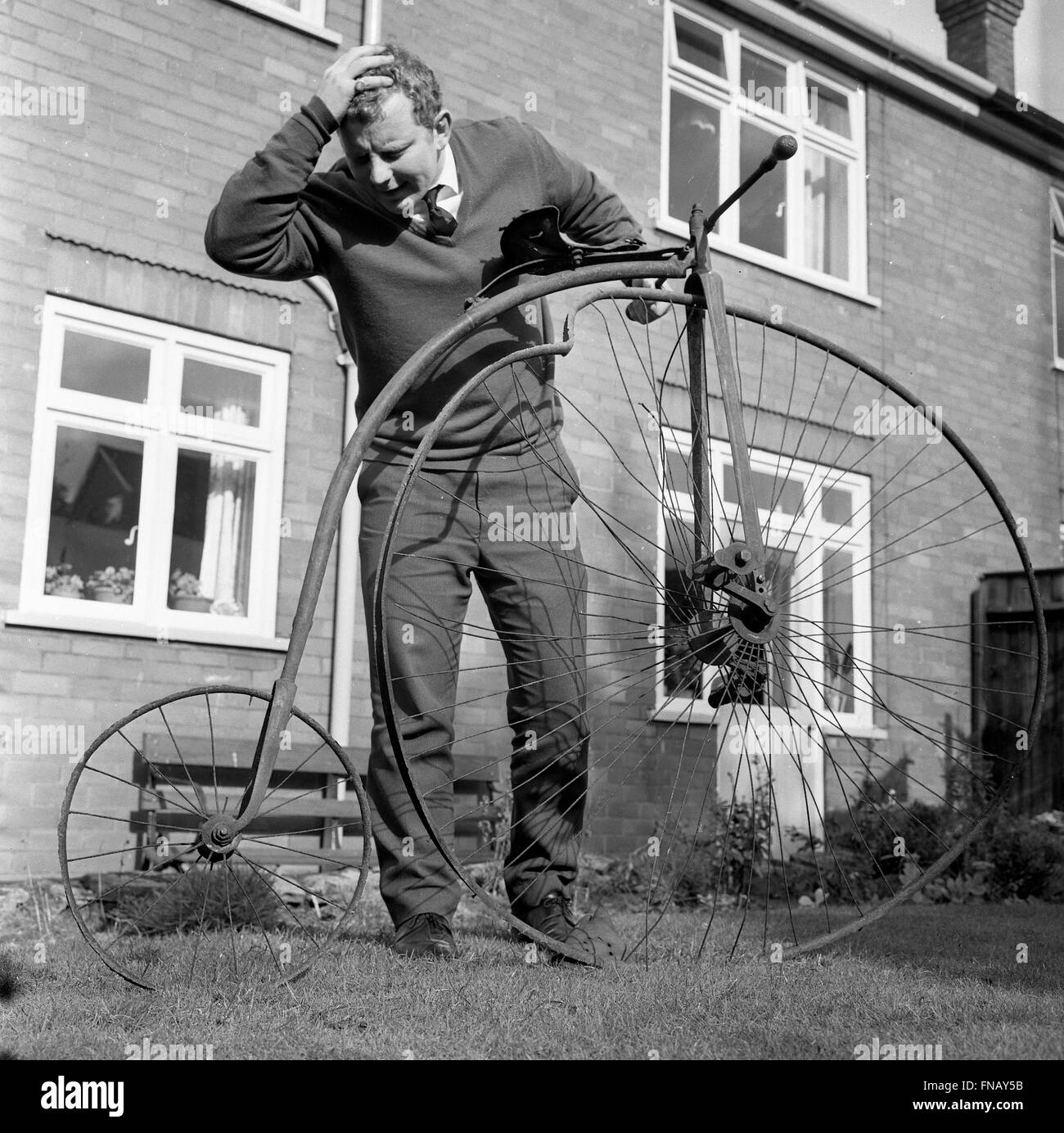 Man with penny farthing bicycle in need of repair with a buckled wheel 1960s Stock Photo