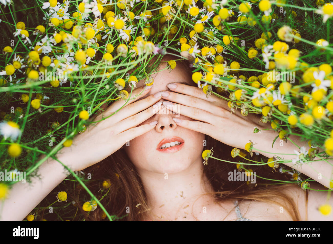 Portrait of young girl with hands on eyes and freckles in chamomile ...