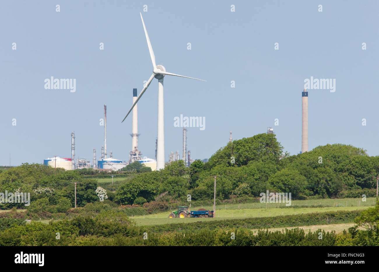 On shore wind turbine and Milford Haven oil refinery and tractor in field in countryside,Pembrokeshire,West Wales,Wales,U.K. Stock Photo