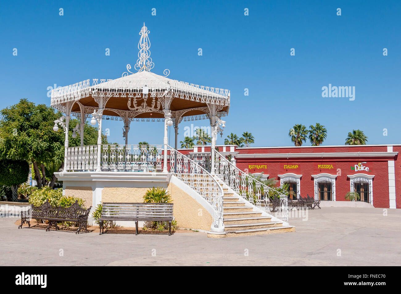 The kiosko or gazebo in San Jose del Cabo's main square in Old Town, with benches beside and colorful red restaurant behind. Stock Photo