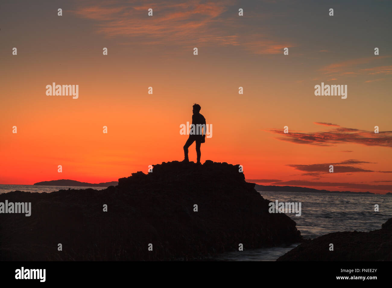 Silhouette of a man at sunset on a rock jetty at Shaw’s Cove in Laguna Beach, Southern California Stock Photo