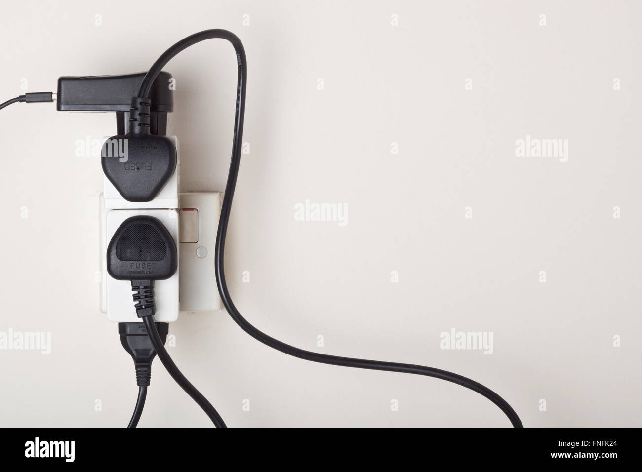 Many power cables plug into an ac power outlet on a wall Stock Photo