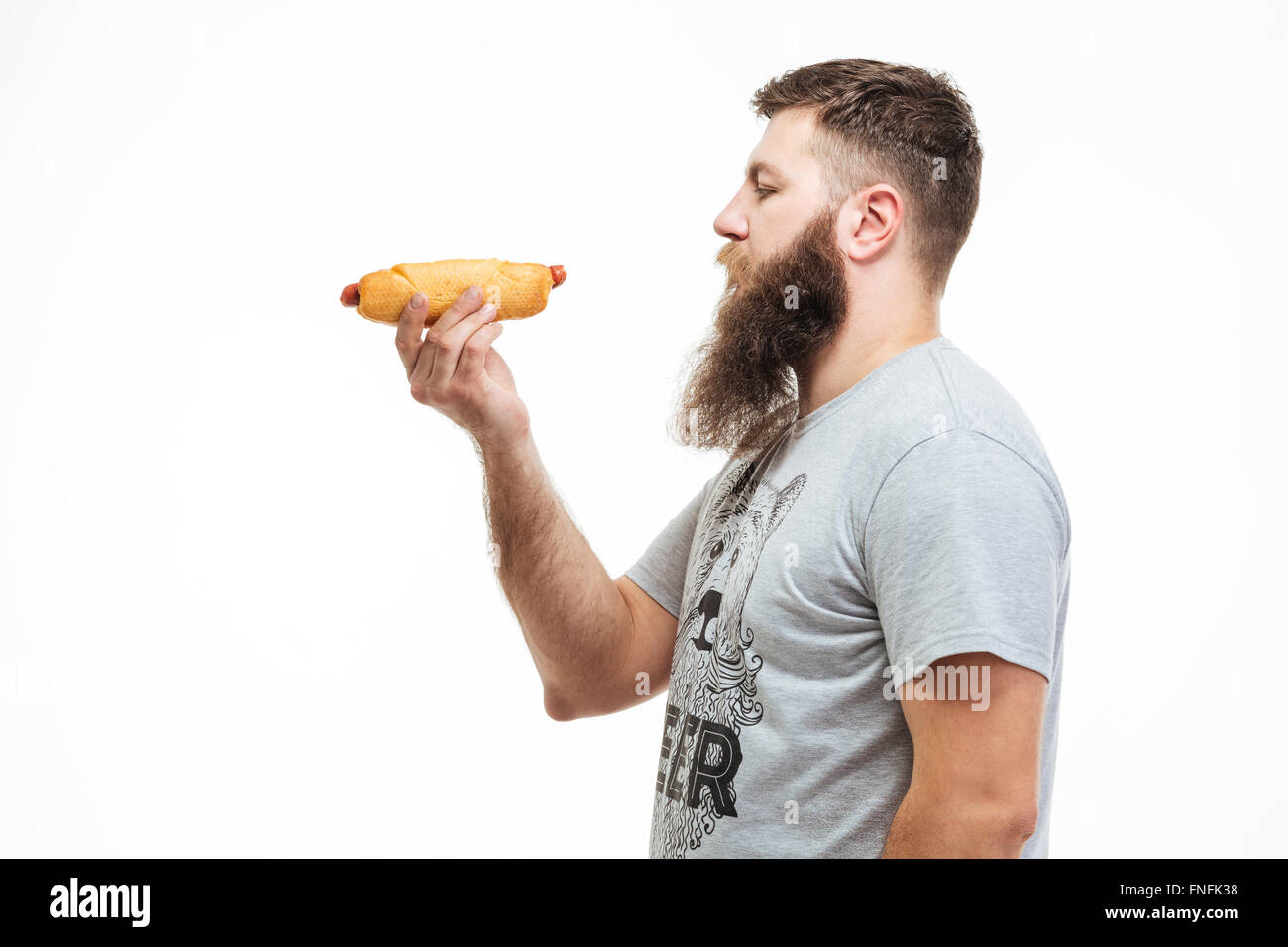 Profile of attractive bearded man standing and holding hot dog over white background Stock Photo