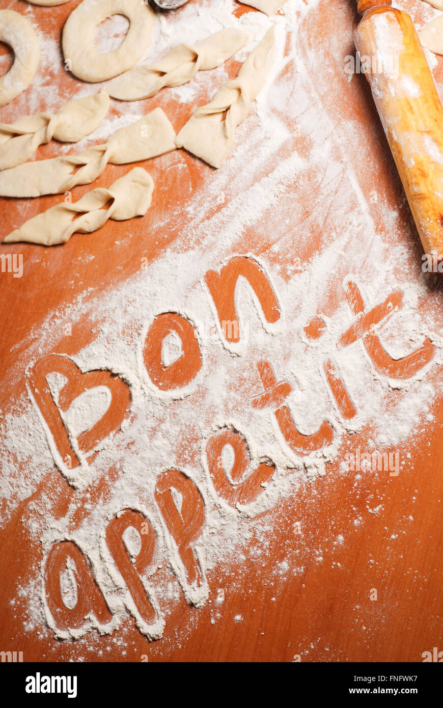 The inscription bon appetit on the table with flour , dough and donuts