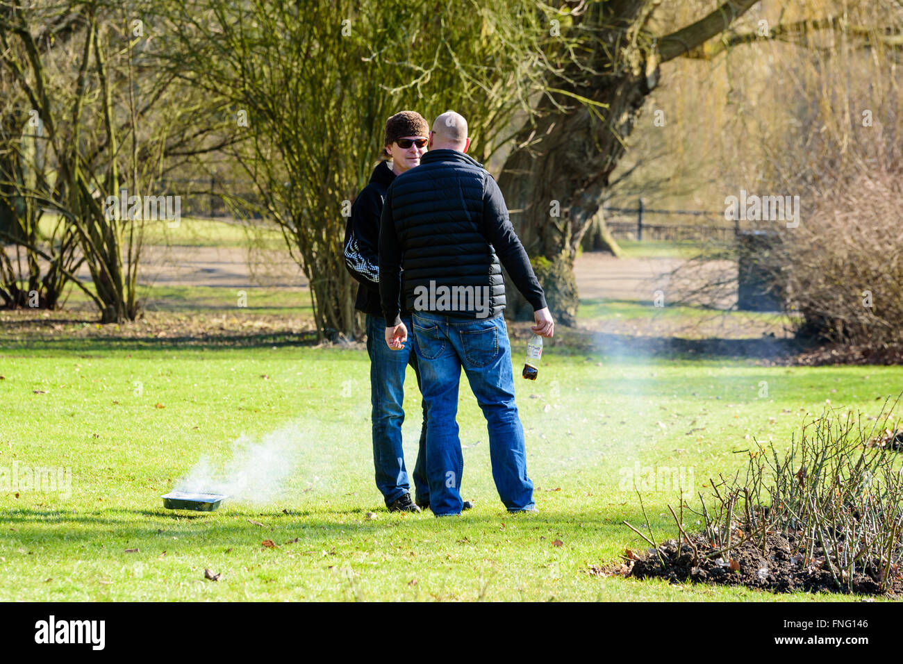 Lund, Sweden - March 12, 2016: Two males are having a conversation in the park. Beside them is a disposable grill on the lawn. R Stock Photo