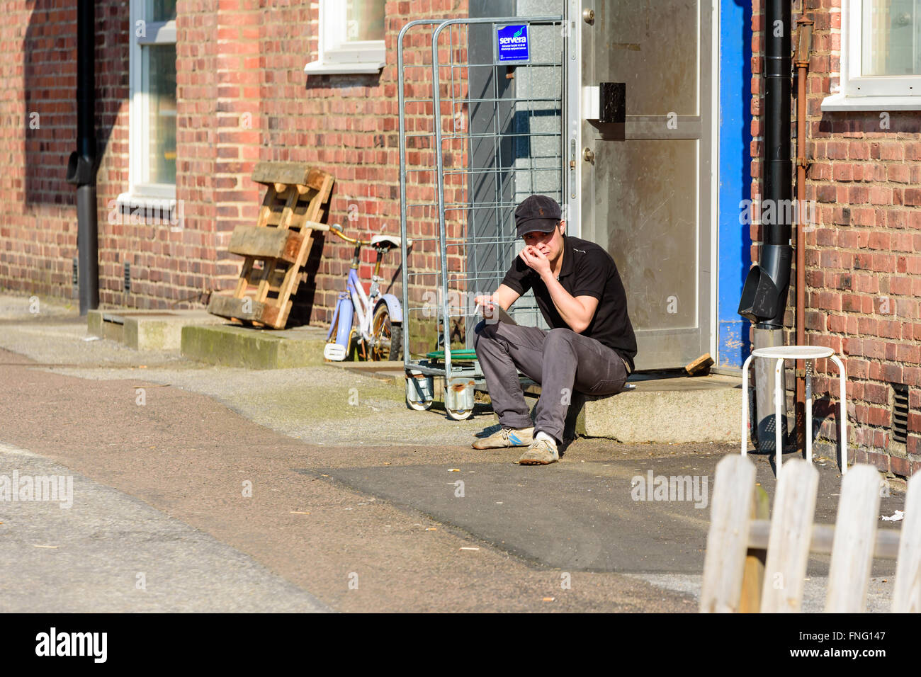 Lund, Sweden - March 12, 2016: Young male adult is having a break and a smoke outside the back entrance to a restaurant. He sits Stock Photo