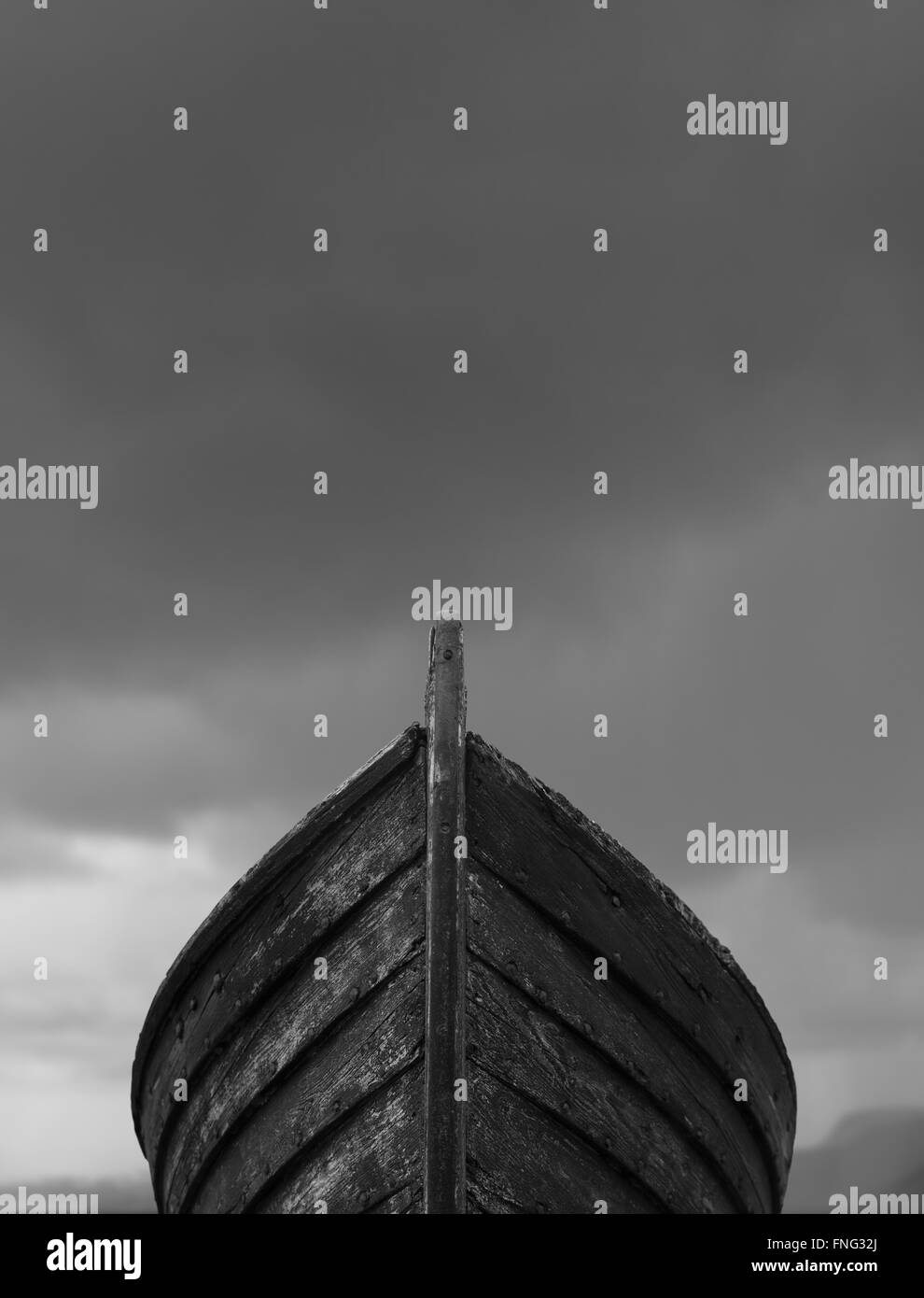 Vertical front view of an old fishing wood boat with rusted nails with dramatic grey storm clouds in the background Stock Photo