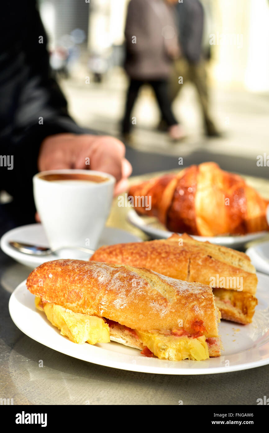man sitting in a table in the terrace of a cafe set for breakfast, with some cups of coffee, a croissant and a spanish omelette Stock Photo