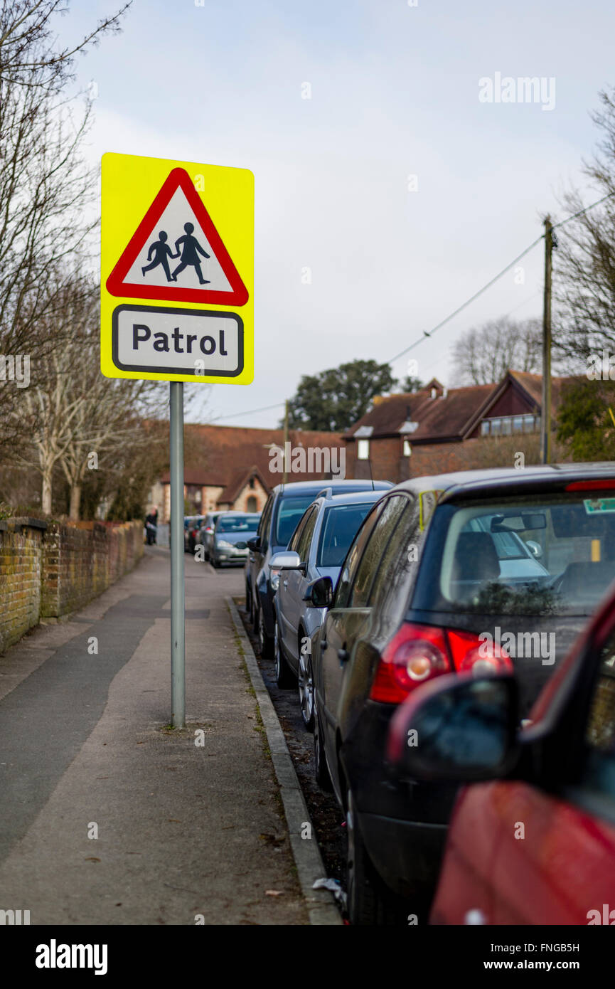 School crossing patrol sign by a potential hazard of parked cars opposite an Infant school in Petersfield Hampshire Stock Photo