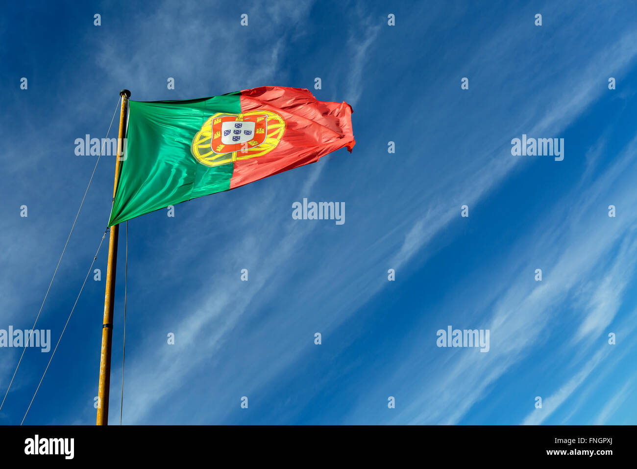 portugal flag od flagpole with blue sky with little clouds in the background Stock Photo