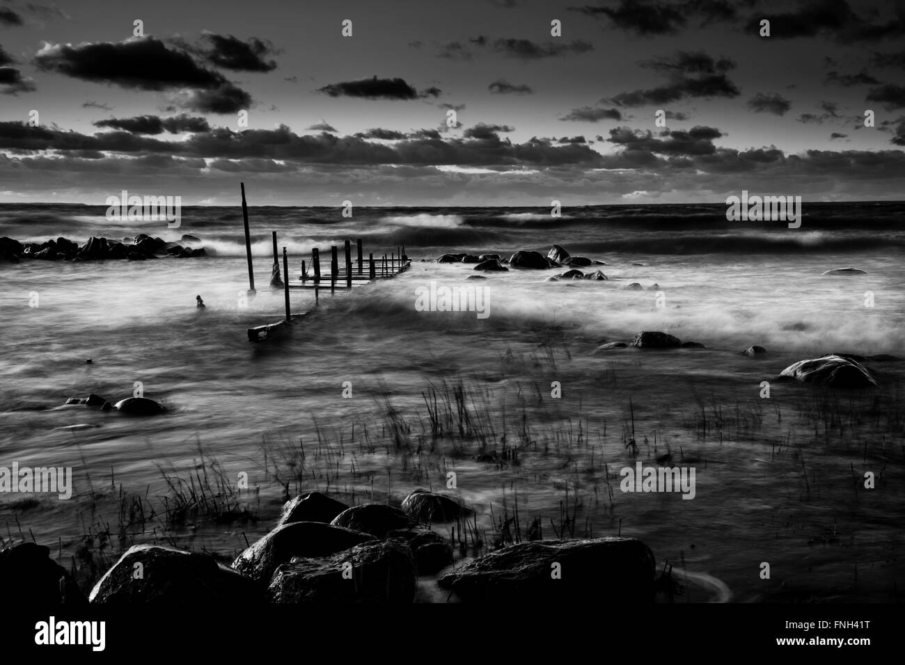Old bridge in stormy sea. Gloomy sunset in rocky beach.  Wild and natural environment. Black and white. The baltic sea Stock Photo