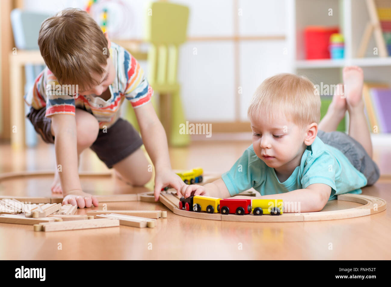 Cute children playing with wooden train. Toddler kids play with blocks and trains. Boys building toy railroad at home or daycare. Stock Photo