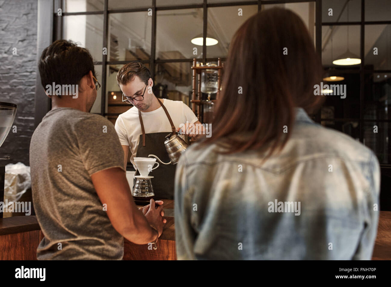 Couple at a cafe counter with barista pouring coffee Stock Photo