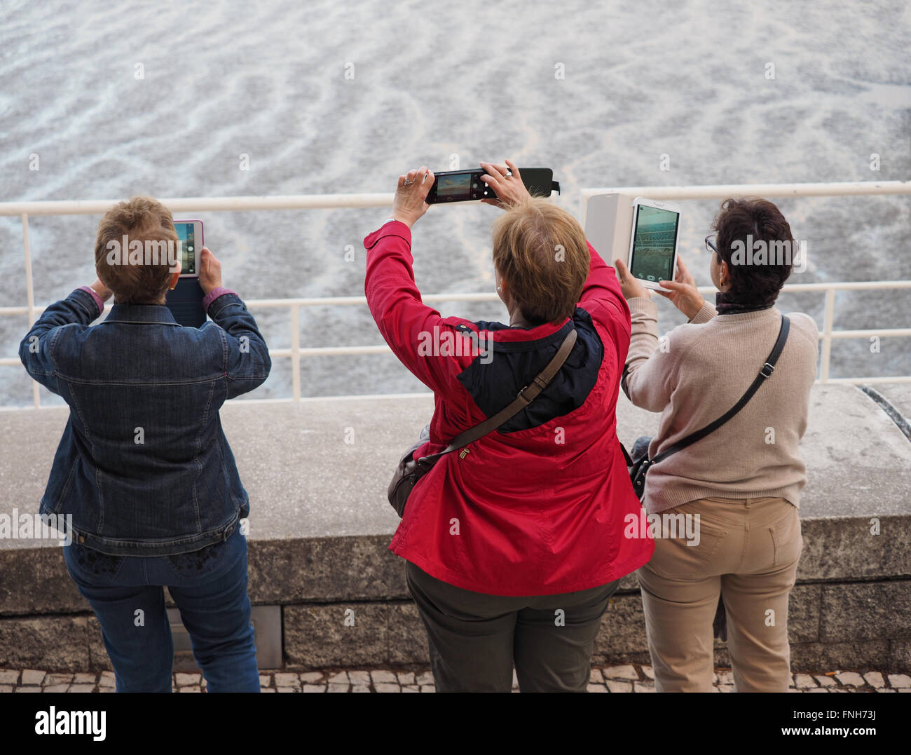 Three middle-aged women taking pictures with their mobile devices Stock Photo