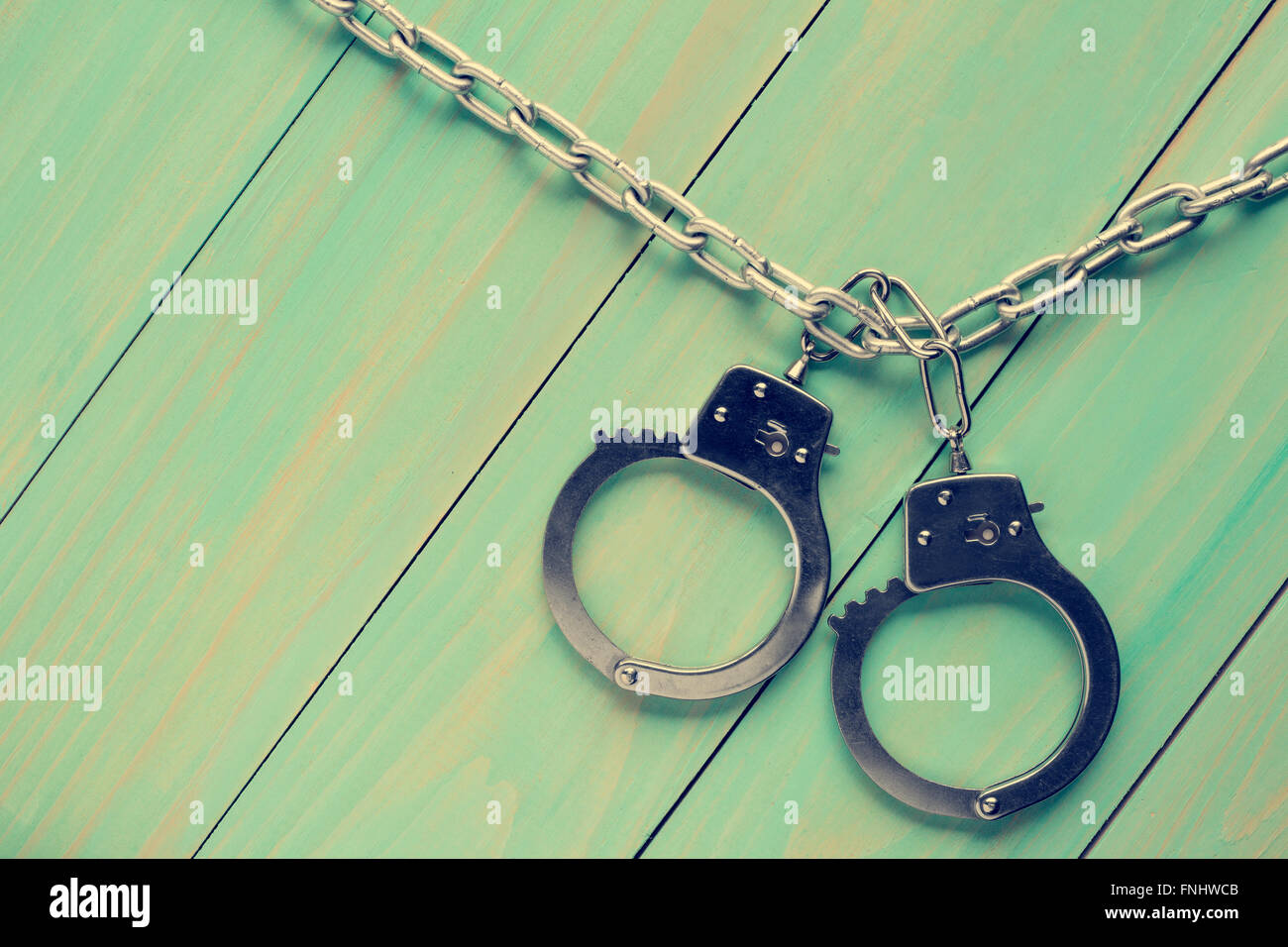 Handcuffs hanging on the chain against wooden background.Filtered image. Stock Photo