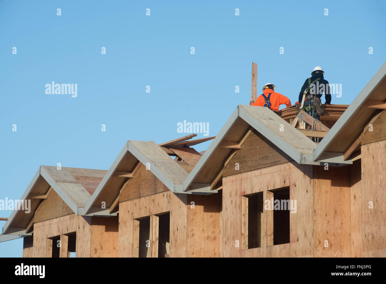 Two workers apply plywood to the top of an apartment under construction. Stock Photo