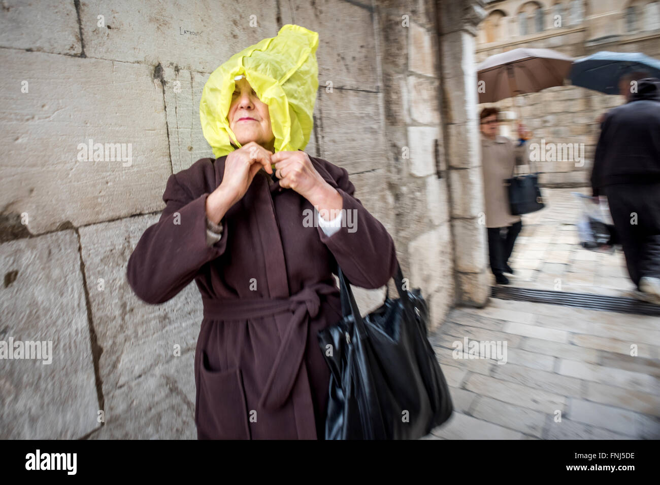 A visitor using a bag to take shelter from a downpour in the old city of Dubrovnik. Stock Photo