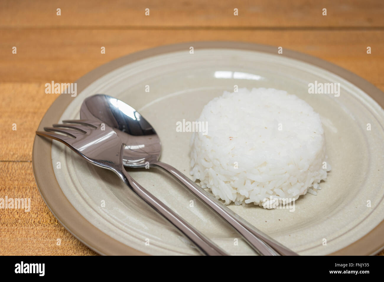 Cooked rice and spoon and fork on plate on wooden table Stock Photo Alamy