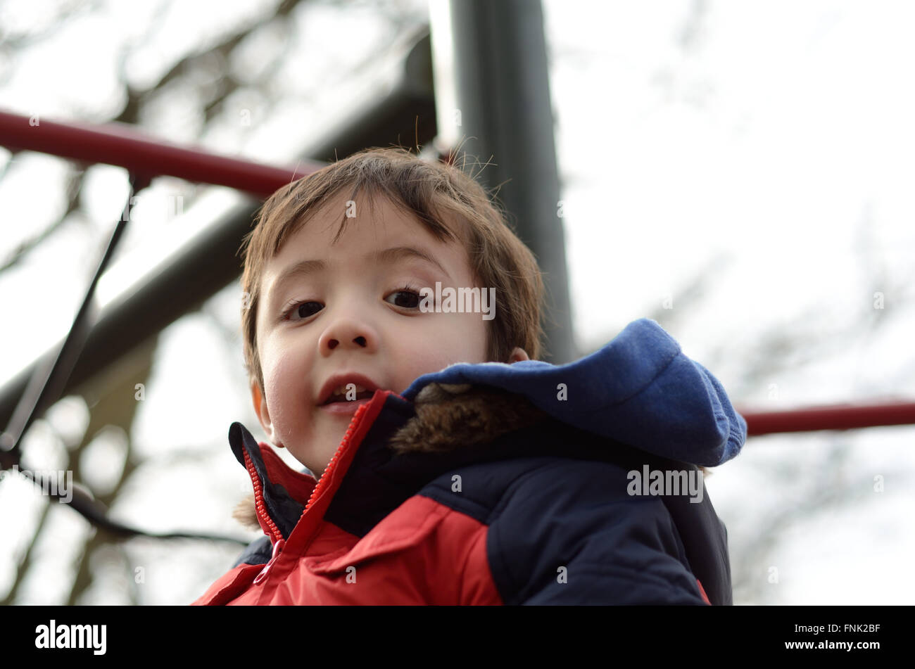 Looking up at a young boy who's standing on a climbing frame in the park Stock Photo