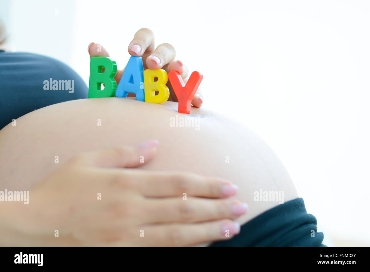 Young expectant mother with letter blocks spelling baby on her pregnant belly Stock Photo
