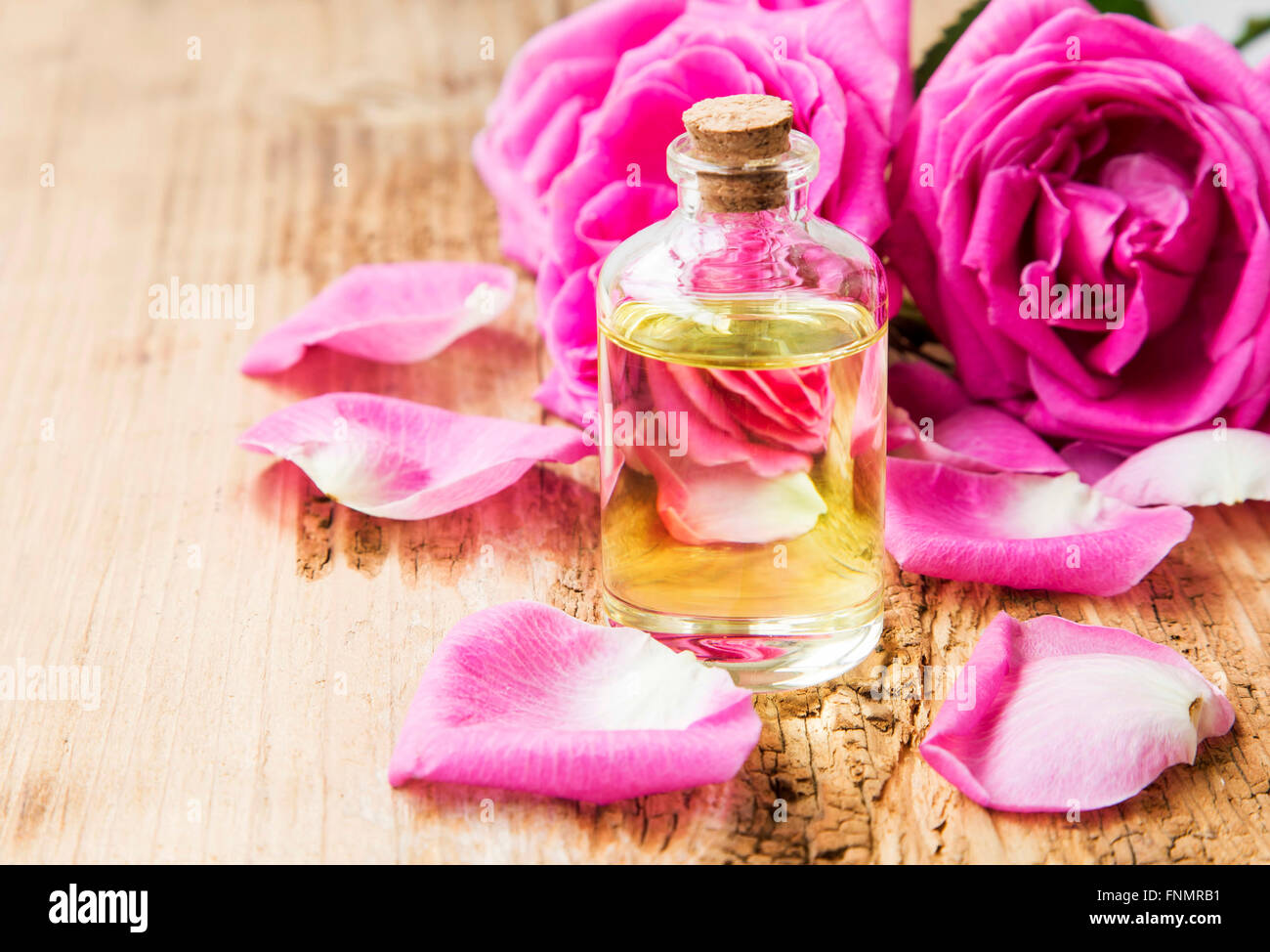 Rose essential oil in a bottle with pink roses and petals on wooden